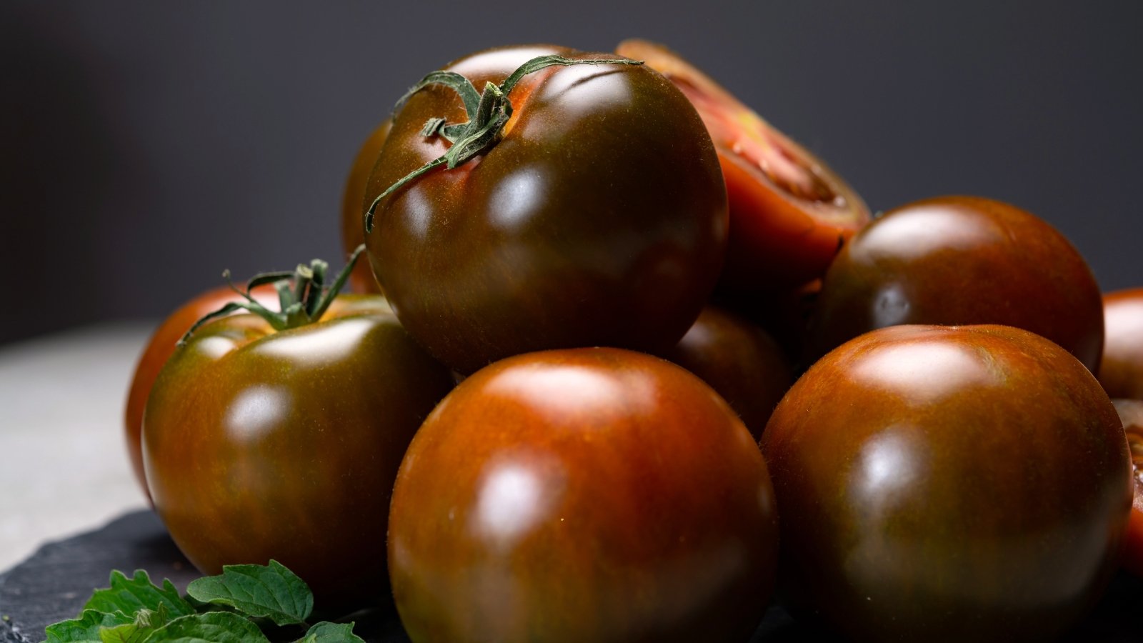 Close-up of ripe fresh deep purple tomatoes with a slight reddish tint on a gray table.