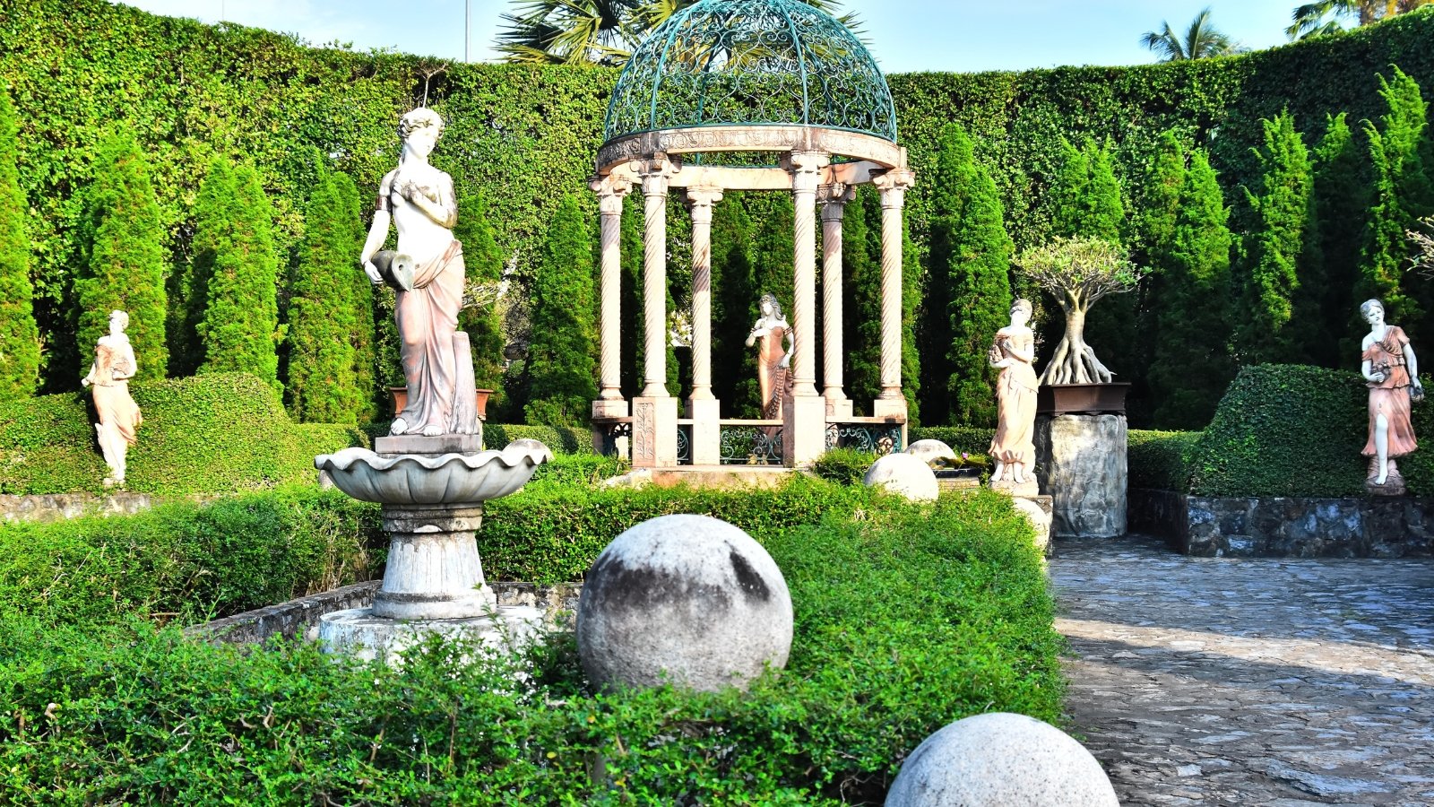 View of the garden with a Marble Gazebo, statues of women delicately adorn the landscape, surrounded by meticulously trimmed boxwood hedges, creating a serene and classical ambiance.