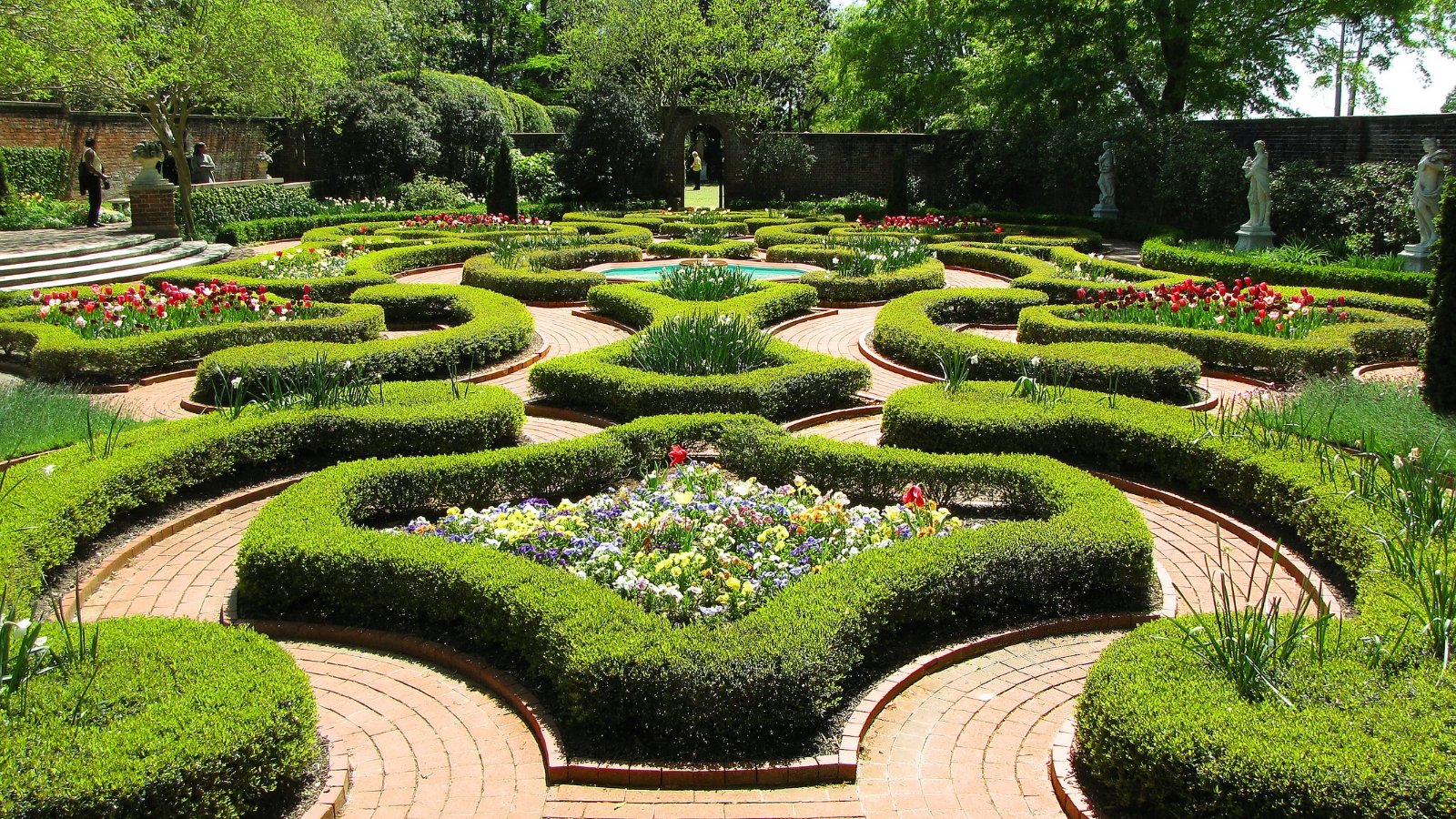 The groomed palace gardens adorning the front passageway to Tryon Palace are characterized by their meticulously maintained flower beds, symmetrical boxwood hedges, and grand allées framed by stately trees.
