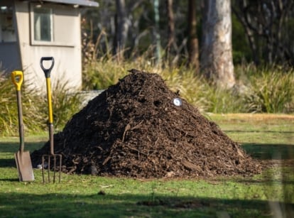 A mound of decomposing plant material sits on grass with a shovel beside it.