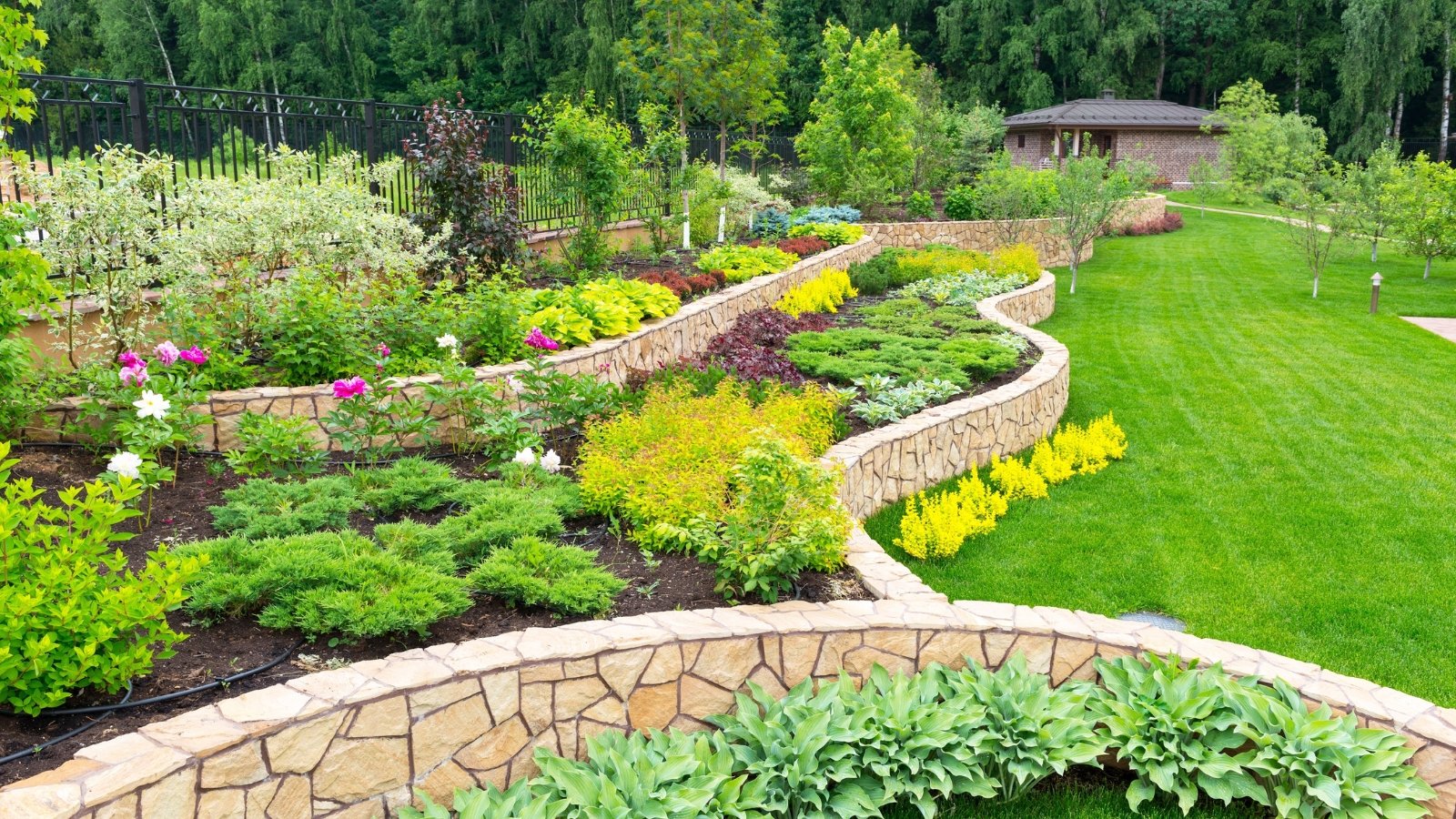 The natural stone landscaping showcases terraces adorned with a myriad of plants and flowers, creating a picturesque and harmonious blend of rugged textures and vibrant colors.