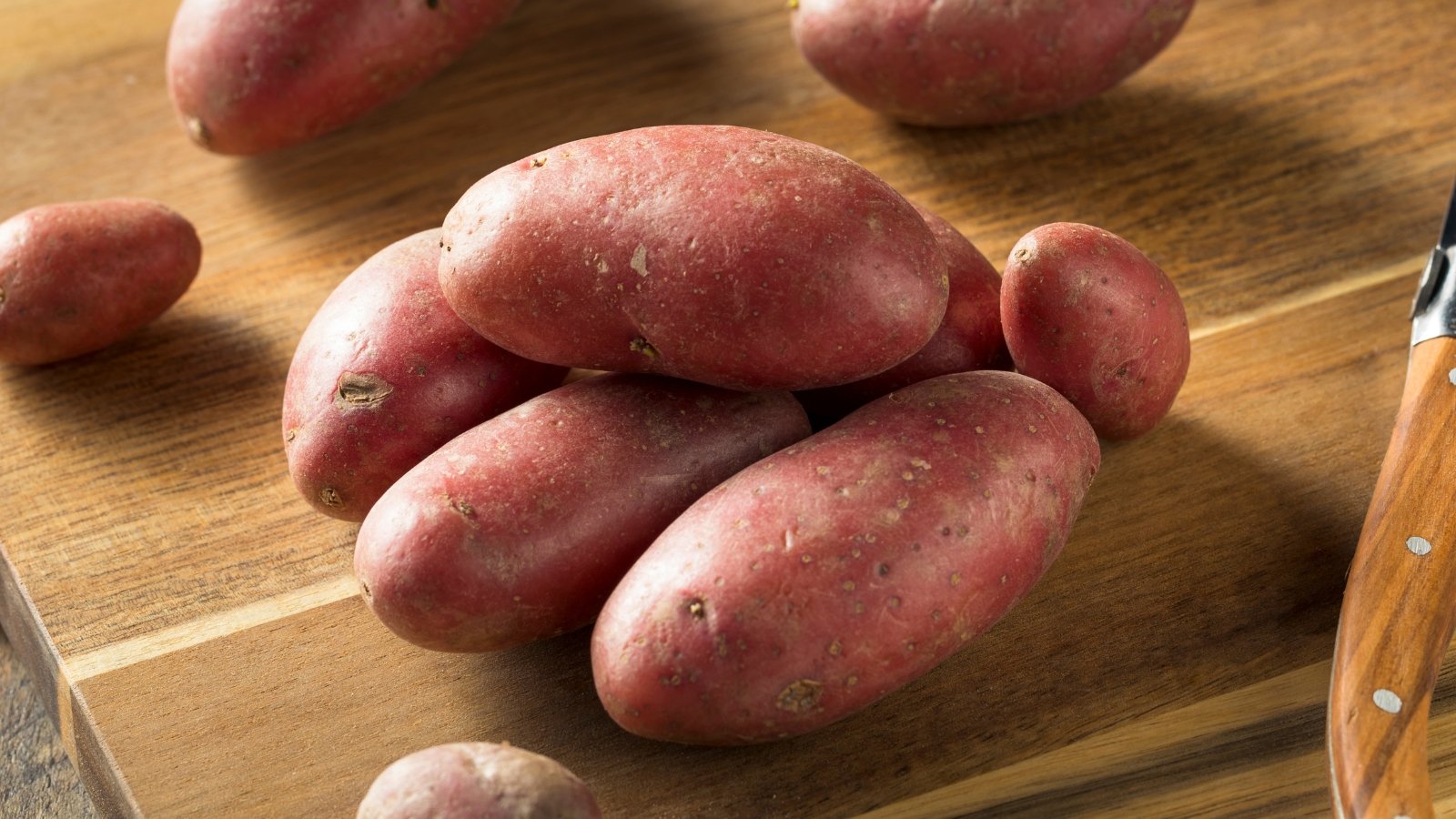 Fresh Amarosa potatoes sit atop a rustic wooden cutting board, their red skins catching the light. The rich hue of the potatoes contrasts beautifully with the natural tones of the board, creating an inviting culinary scene.
