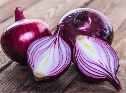 A whole and a halved Allium cepa bulb with glossy outer layers and tightly packed inner rings.